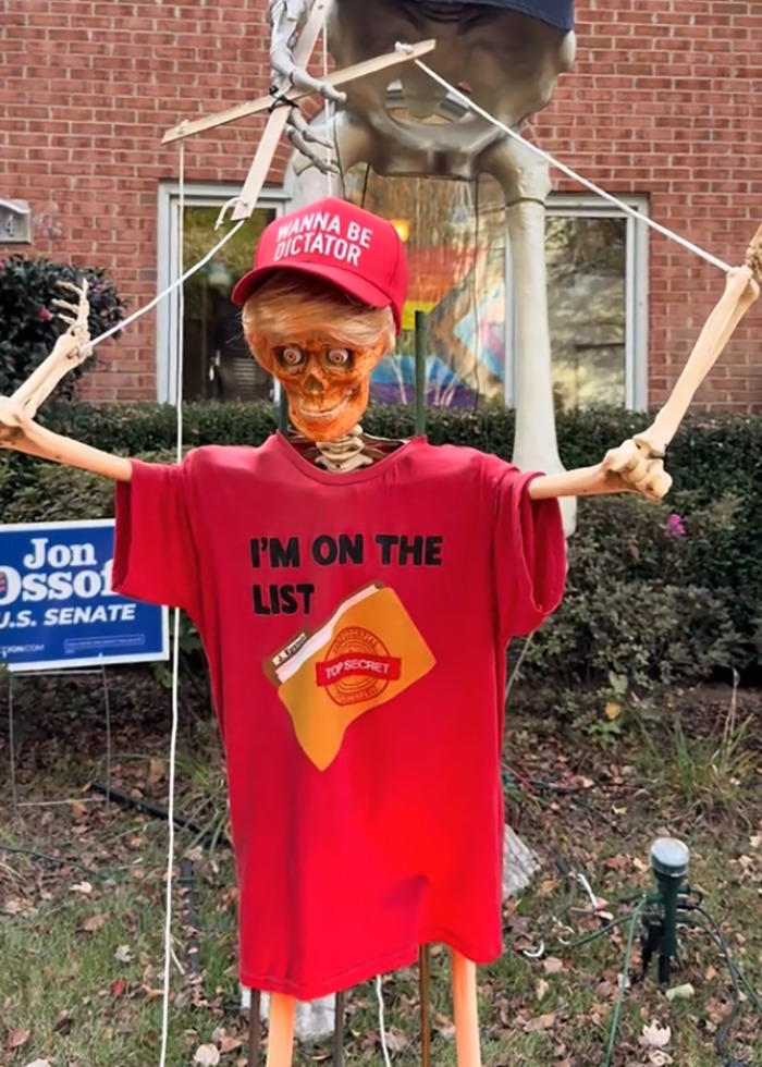 Skeleton Halloween display wearing a red shirt and hat as part of an elaborate anti-MAGA Halloween decoration.