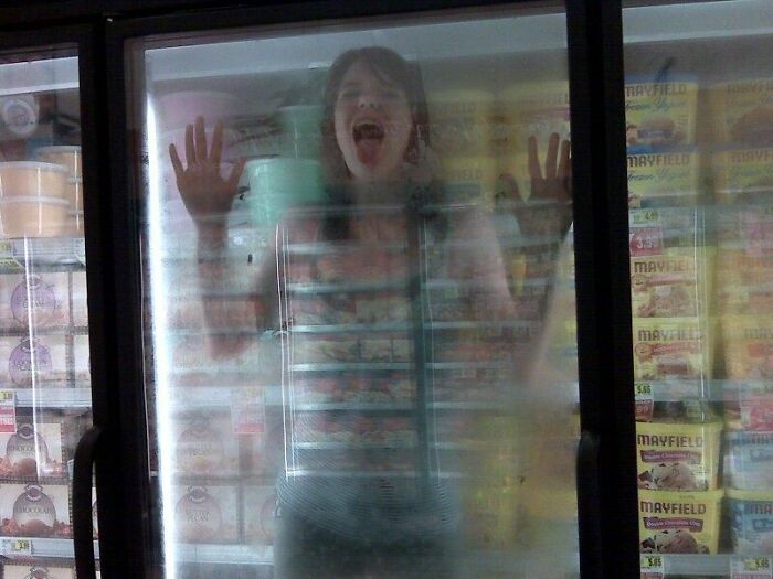 Person pressed against icy freezer door with hands and open mouth, creating a creepy photo moment that chills the viewer.
