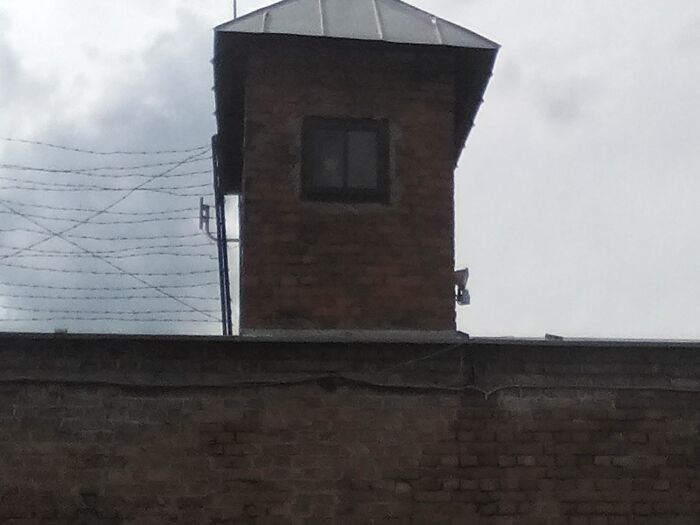 Brick guard tower behind barbed wire fence under a cloudy sky, a creepy photo making hearts skip a beat.