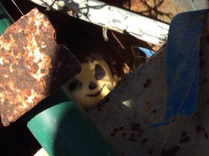Creepy photo of a sinister mask partially hidden among rusty metal and debris, evoking eerie and unsettling feelings.