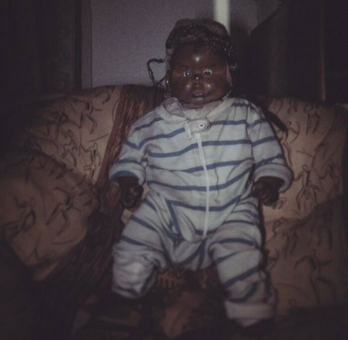 Creepy photo of a dark doll in striped pajamas sitting on a patterned chair, evoking unsettling feelings and eerie vibes.