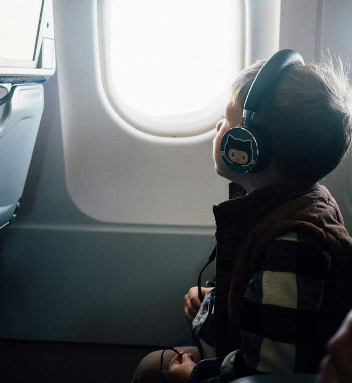 Child wearing headphones looks out airplane window during a long flight, reflecting the teen refusing to entertain a stranger&rsquo;s kid.