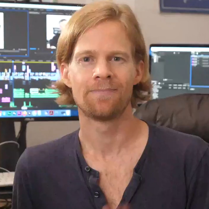 Man behind blinking guy GIF with red hair and beard sitting in front of computer screens in a casual home office setting.