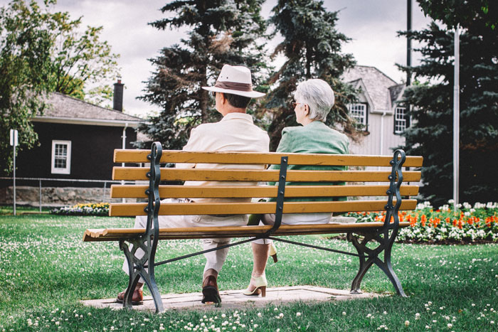 Elderly parents sitting on a park bench, symbolizing a 19YO choosing his parents over his 27YO girlfriend.