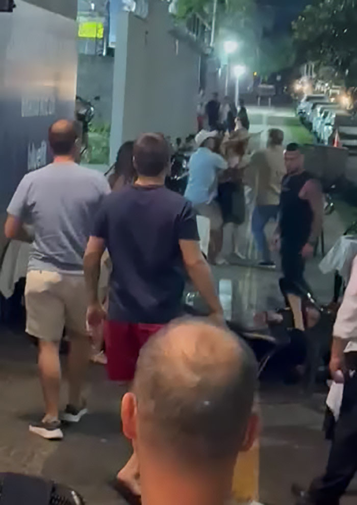 A group of people gathered at night, man intervening as a woman throws a chair at a kid, children come first debate.