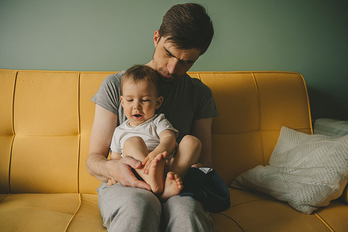 Man sitting on a couch holding his young son who has no idea about his real parents in a cozy home setting.