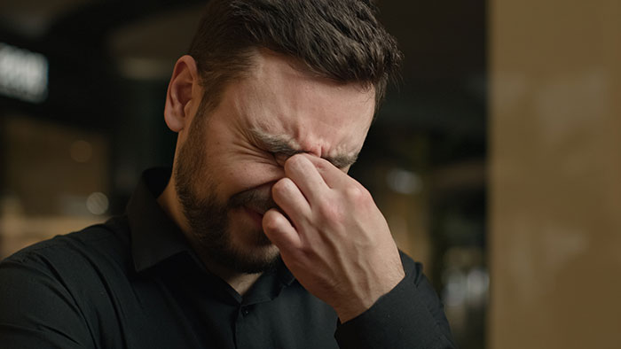 Man with beard looking distressed, holding his face, contemplating telling his son the truth about his real parents.