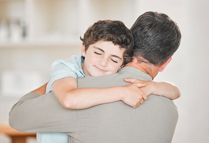 Man hugging boy who has no idea about his real parents, showing a tender moment between them indoors.
