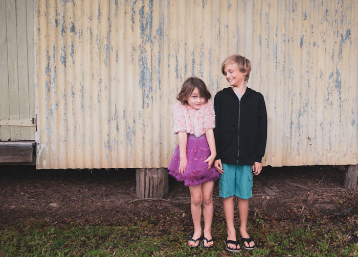 Two children standing outside, a girl in a purple dress and a boy in a black hoodie, representing sibling dynamics.