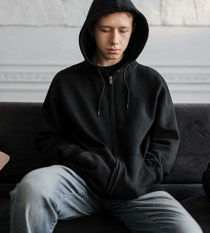 Teenage son in black hoodie sitting with a downcast expression, reflecting parents spoiling daughter and neglecting him.
