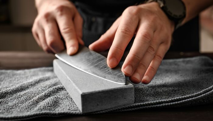 Person sharpening a knife on a stone with focused hands showing simple car stuff skills and maintenance techniques.