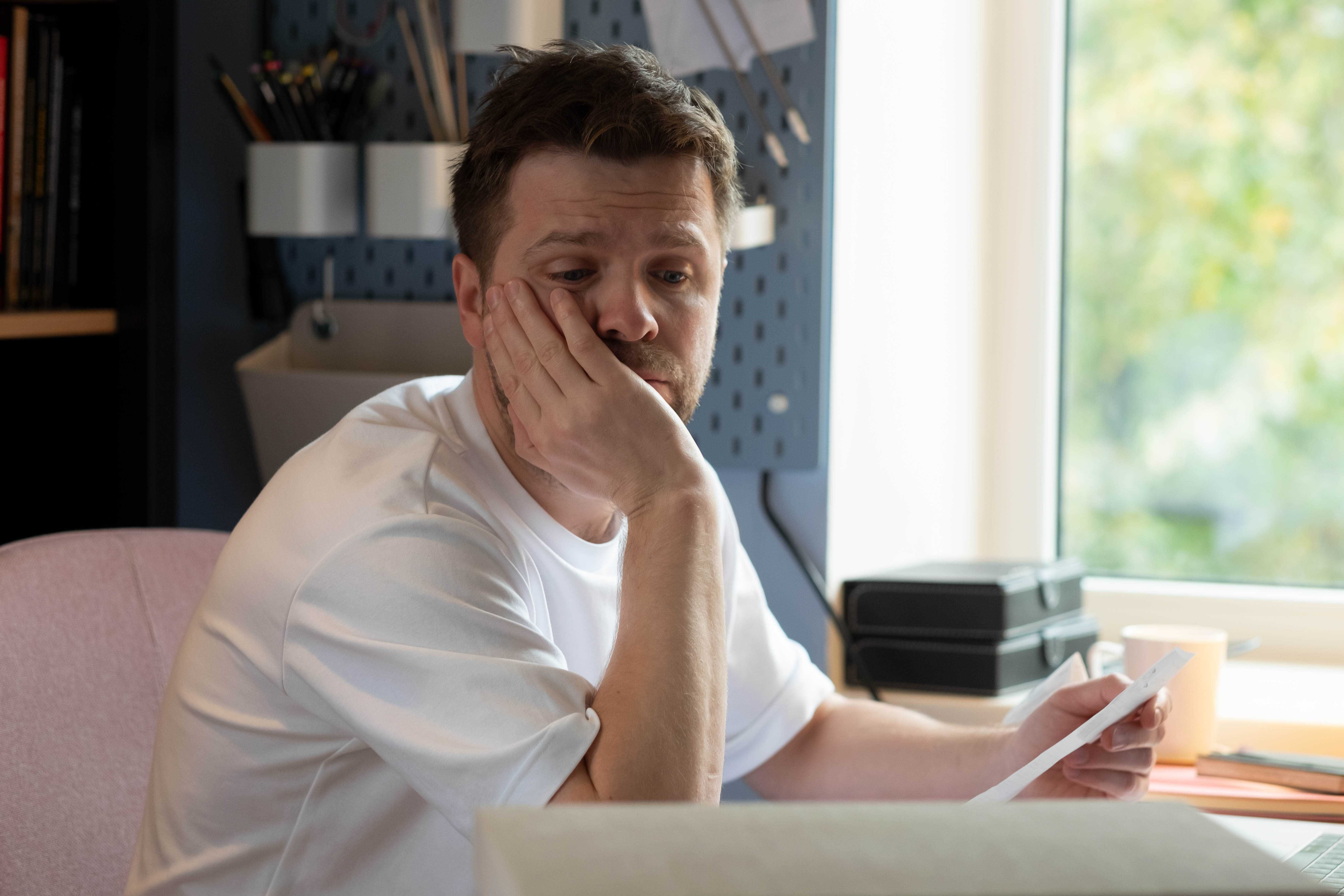 Man looking worried at a letter with hand on face, reflecting on woman going to gala with client as date situation.