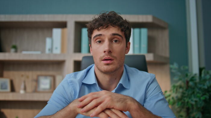 Young male accountant in a blue shirt sitting at desk in office, sharing engaging stories that prove accounting is not boring.