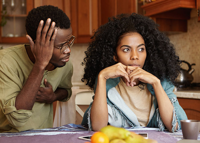 Couple having a tense conversation in a kitchen, woman looking away as man's true colors show during vacation.