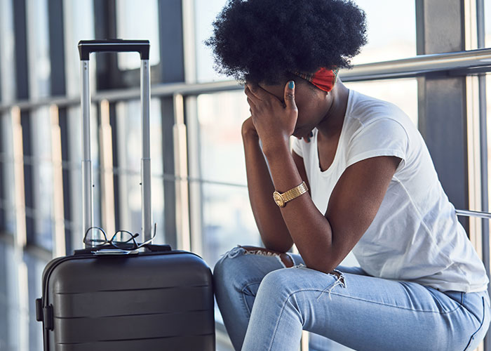 Woman sitting next to suitcase at airport, covering face, reflecting on man&rsquo;s true colors during vacation.