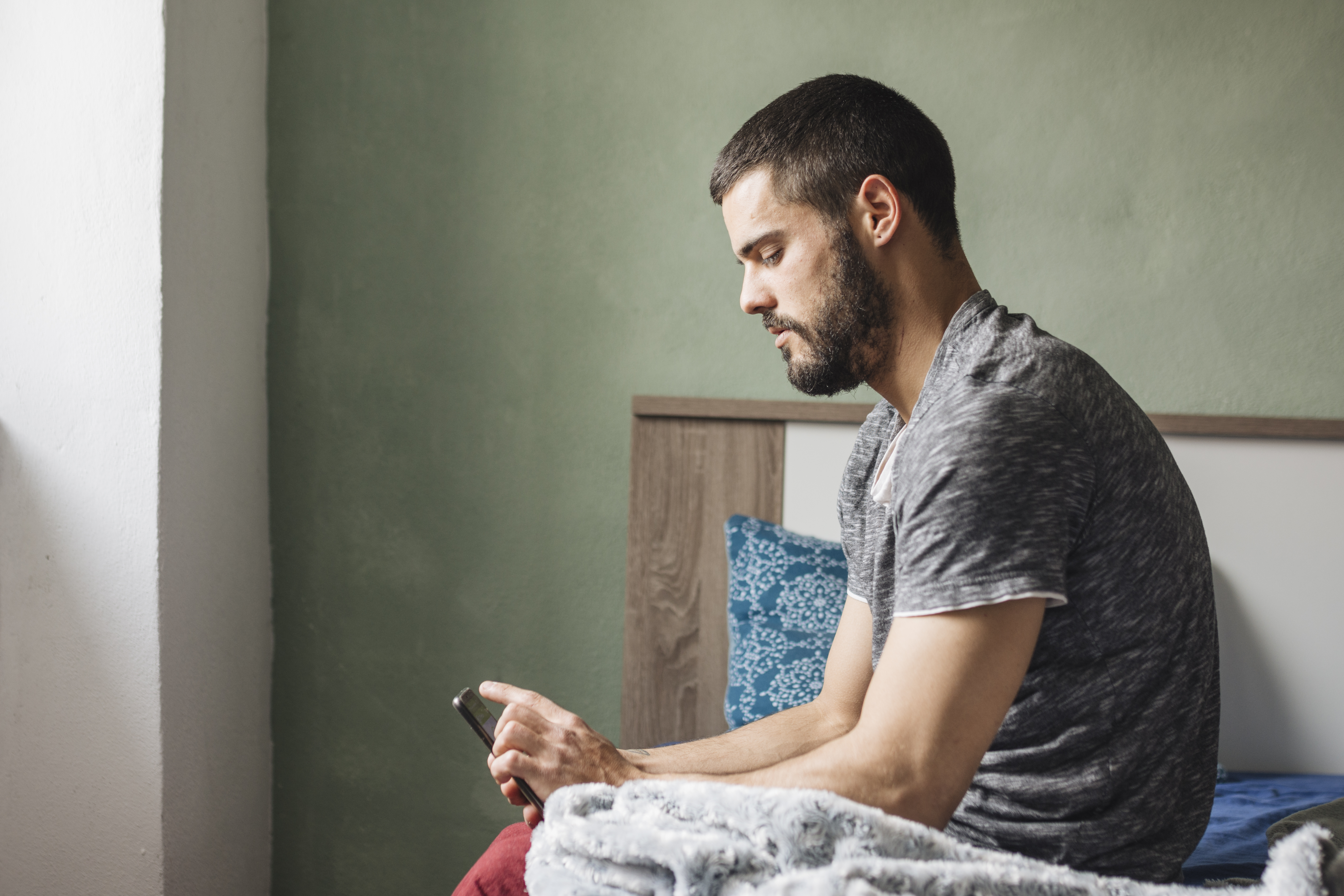 Man sitting on bed looking at phone, reflecting, symbolizing husband questioning everything after woman goes to gala with client.