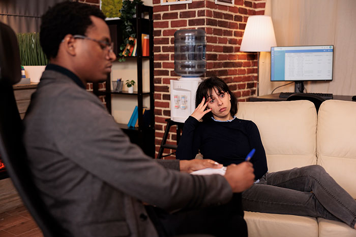 Woman looking distressed during a therapy session with a male therapist in a cozy, brick-walled counseling office.