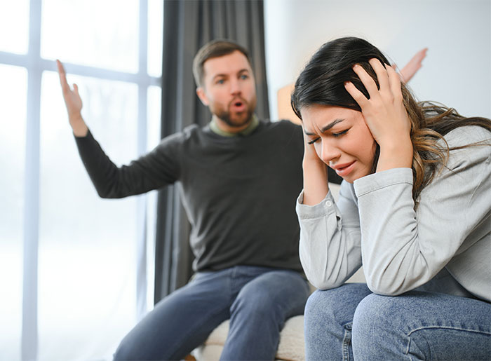 Couple in a heated argument at home, woman distressed while man gestures expressing frustration in a tense relationship moment.