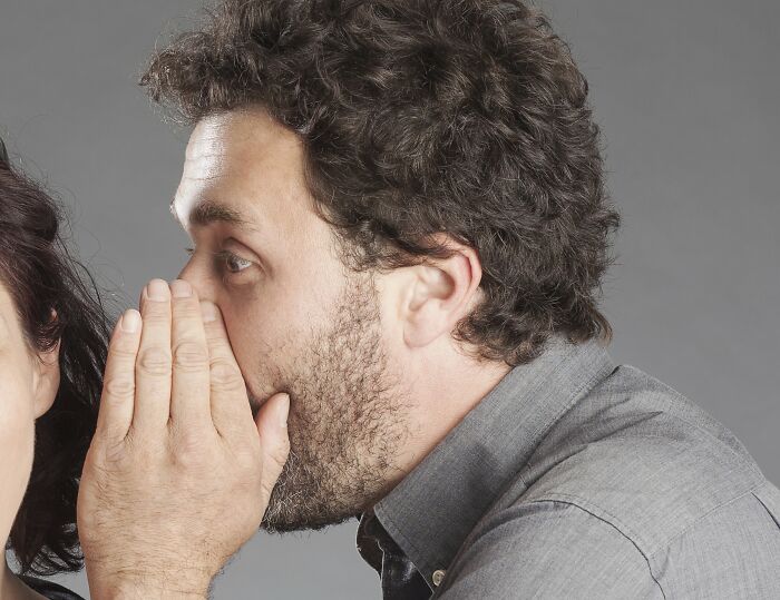 Man whispering a disturbing secret to a woman, illustrating creepy things folks were told and only later realized.