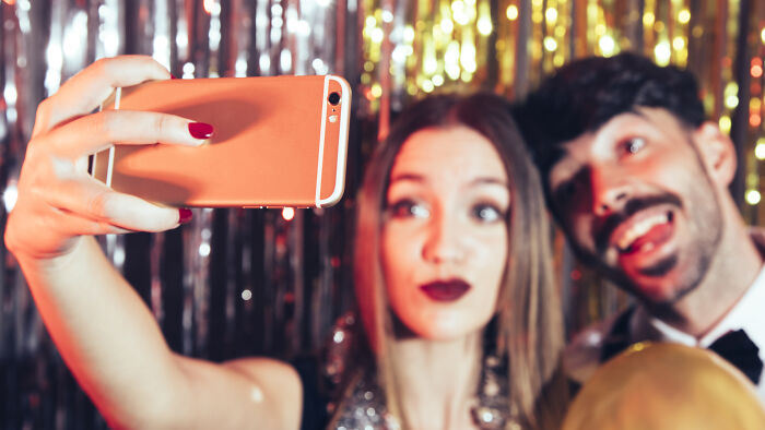Young woman and man taking a selfie at a party, related to boss wife claim affair and innocent worker topics.