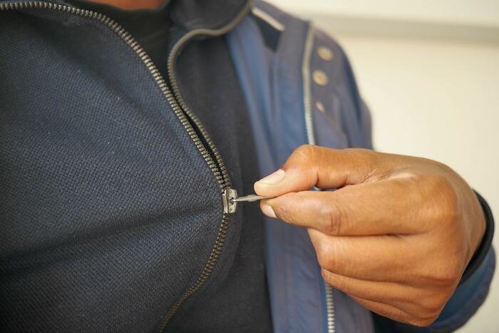 Close-up of a person’s hand fixing a zipper on a jacket, demonstrating simple car stuff skills with minimal training.