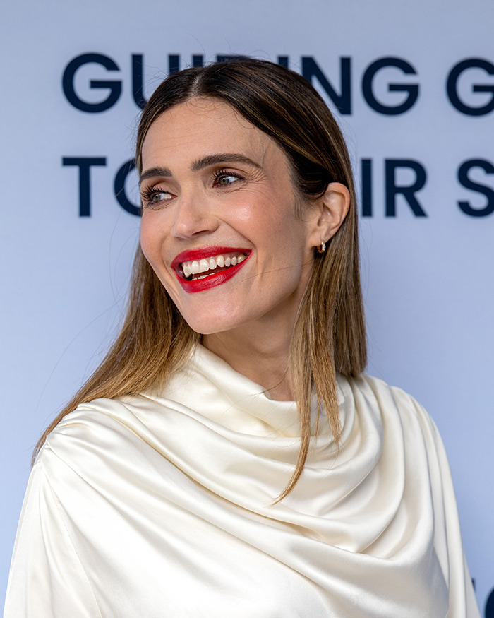 Mandy Moore smiling with red lipstick and sleek hair in a white satin outfit, showing her new unrecognizable look.
