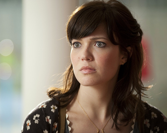Mandy Moore with dark hair and floral top showing an unrecognizable new look that baffles fans in a close-up portrait.