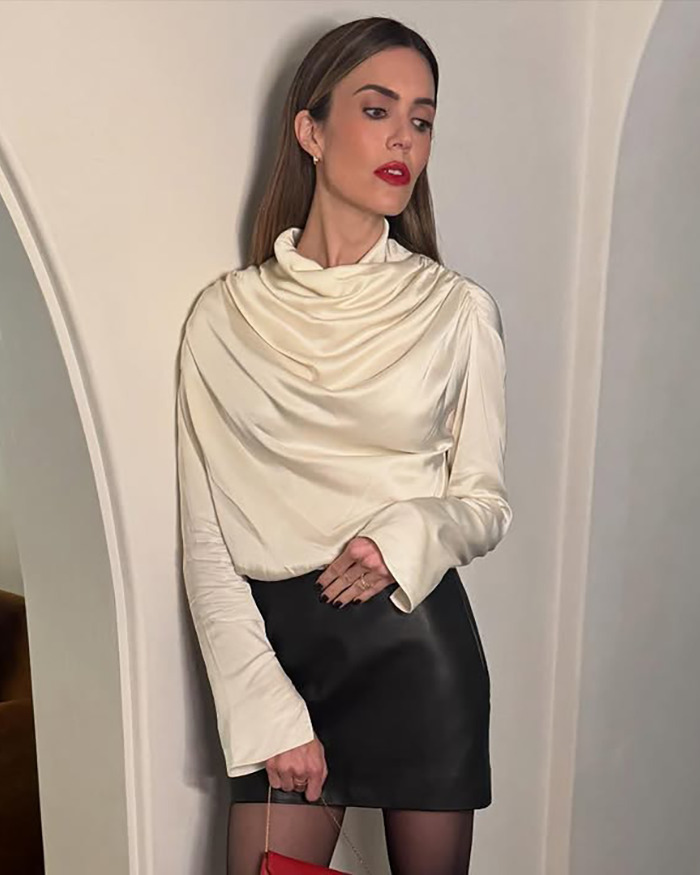 Mandy Moore with an unrecognizable new look wearing a cream blouse and black skirt, posing indoors against light walls.