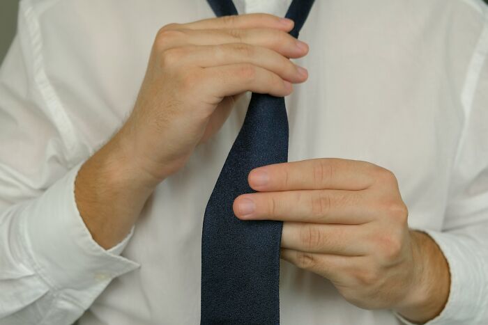 Person in white shirt tying a navy blue necktie demonstrating simple car stuff skills with minimal training.