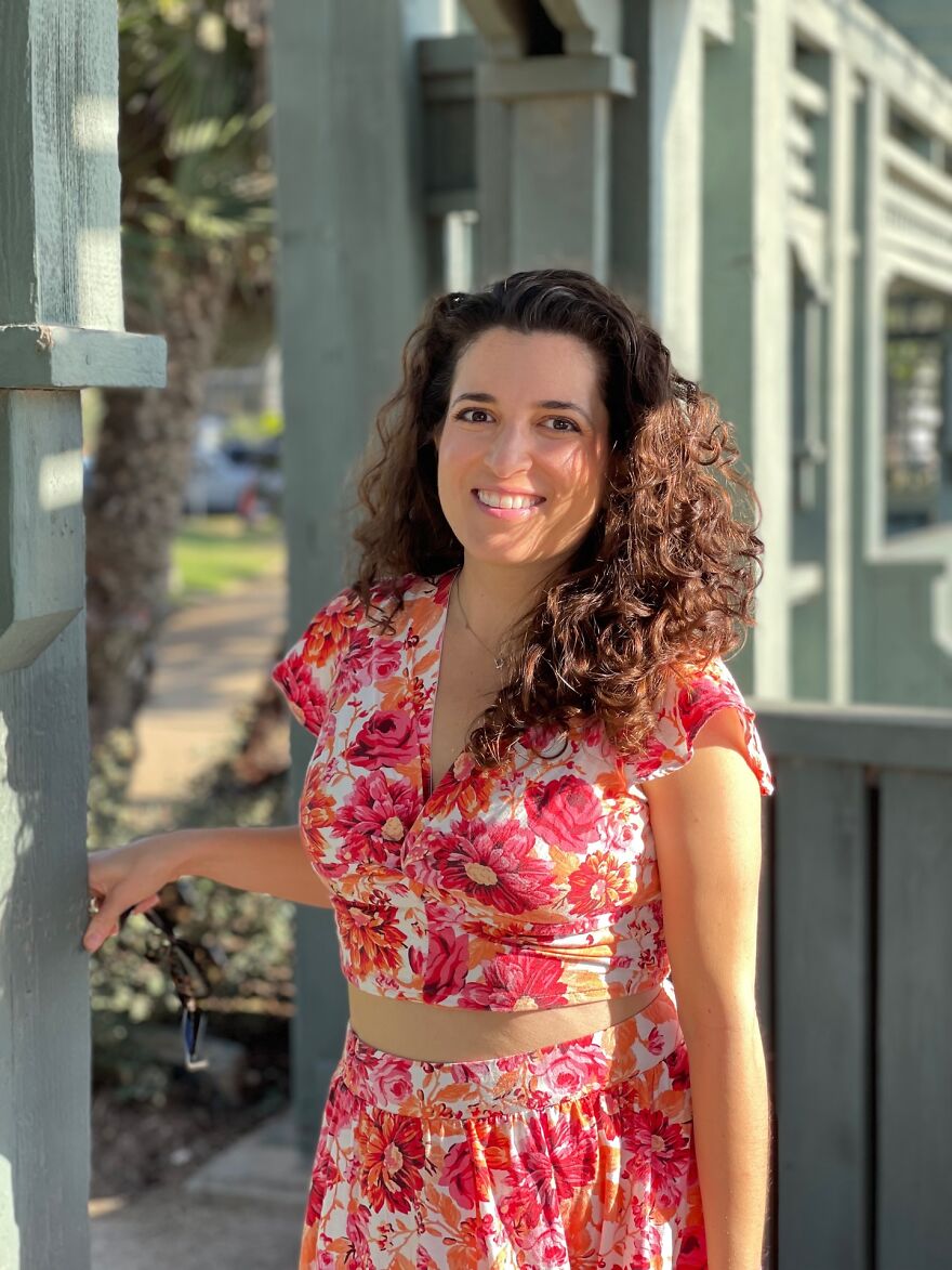 Woman with curly hair and floral outfit smiling outdoors, featured in billboard campaign to find love.