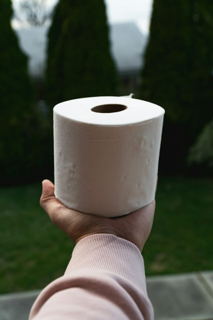 Hand holding a roll of toilet paper outdoors, illustrating funny moments people embarrassed themselves hilariously.