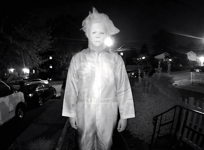 Person wearing a disturbing mask and costume stands on a porch during a doorbell prank at night.