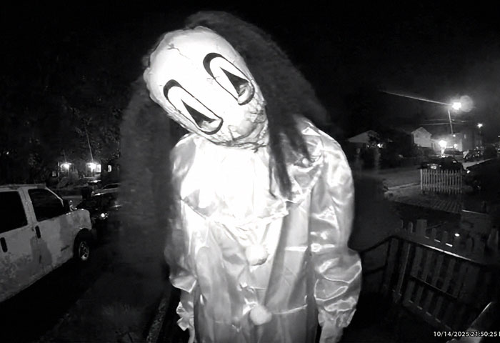 Masked figure in a disturbing doorbell prank captured at night with eerie lighting and neighborhood background.