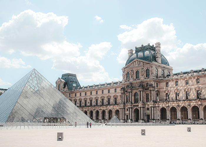 Louvre Museum exterior with glass pyramid entrance under blue sky, referencing notorious jewel thief and smuggling trick.