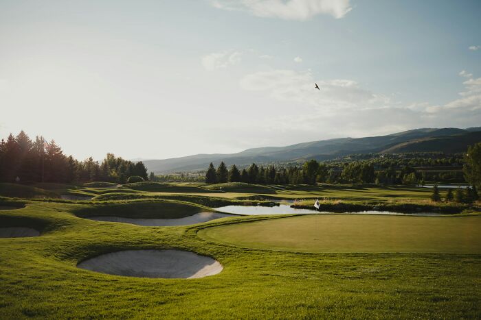 Scenic golf course with sand bunkers and water hazards under a clear sky.