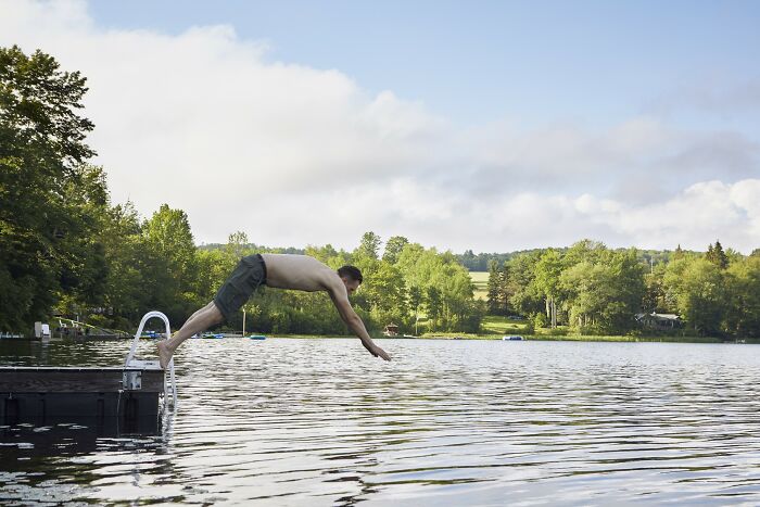 Man diving off dock into lake surrounded by trees, symbolizing simple car stuff skills with maximum results.