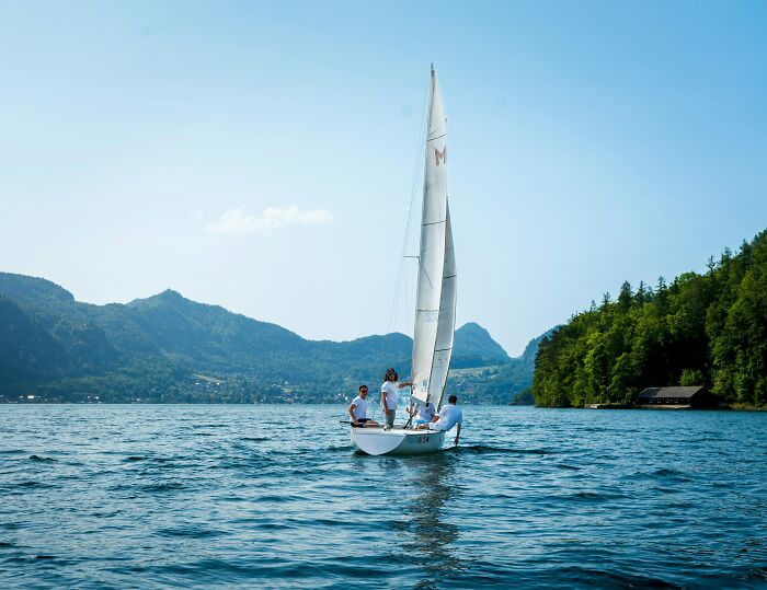 A group of people sailing on a boat in a peaceful lake surrounded by mountains, showing moments universe protected them.