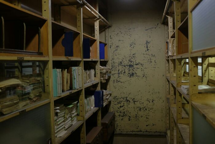 Dimly lit storage room with shelves full of disorganized old files and papers.