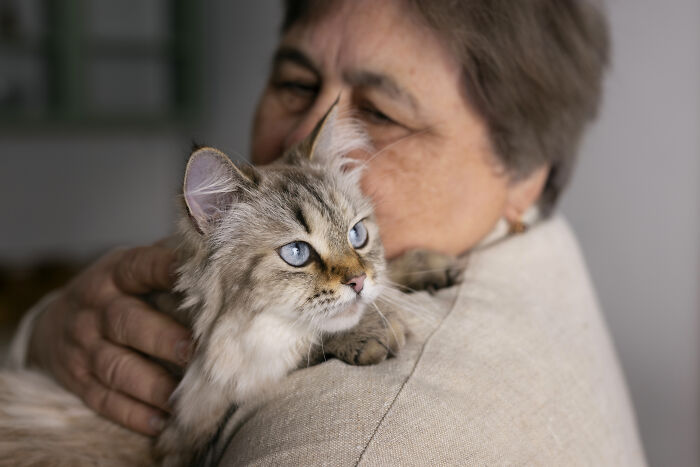 Elderly woman holding a fluffy cat closely, illustrating one of the strangest calls 911 operators received that was true.