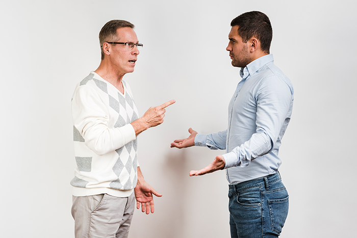 Middle-aged man angrily pointing while arguing with younger man, depicting an obnoxious dinner guest husband dreadful confrontation.