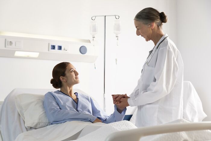 Doctor holding hands with a female patient in hospital bed, showing compassion and support after being protected from harm.