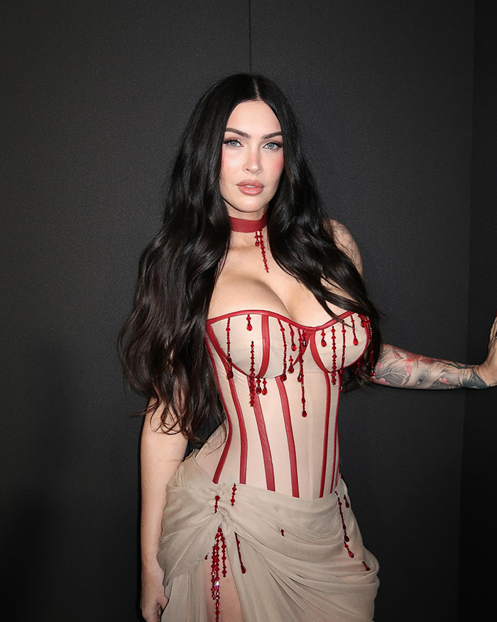 Megan Fox in a sheer corset dress with red accents, sparking plastic surgery speculation at a recent red carpet event.