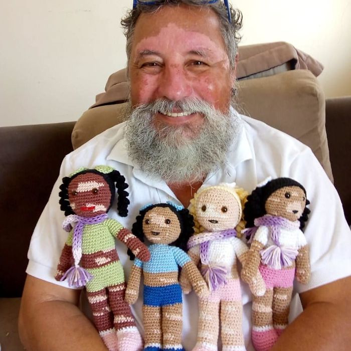 Smiling man holding crocheted dolls, highlighting acts of kindness and men are good in the world.
