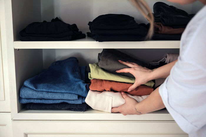 Person organizing folded clothes inside a closet, demonstrating zip-line your boxes out moving advice for easier packing.