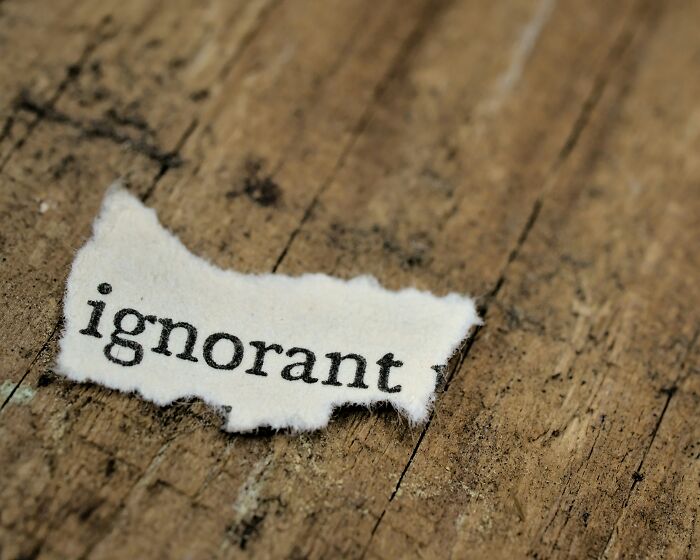 Torn paper with the word ignorant printed on it lying on a wooden surface, related to college courses keyword.