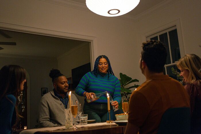 Group of friends sharing relationship advice over dinner with candles, drinks, and a cozy home setting.
