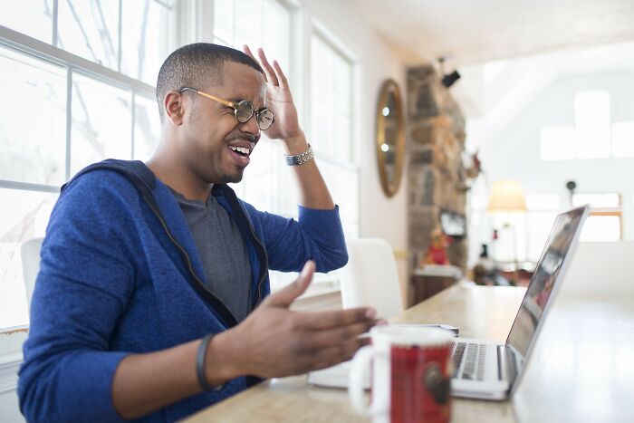 Man frustrated while using laptop at home, illustrating people who lost their jobs to AI and sharing their experiences.