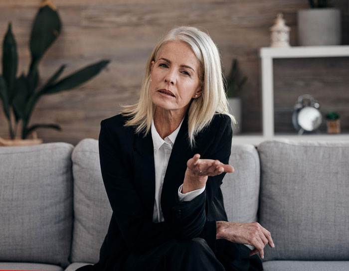 Middle-aged woman in business attire sitting on a couch looking frustrated reflecting rude MIL behavior and family conflict.