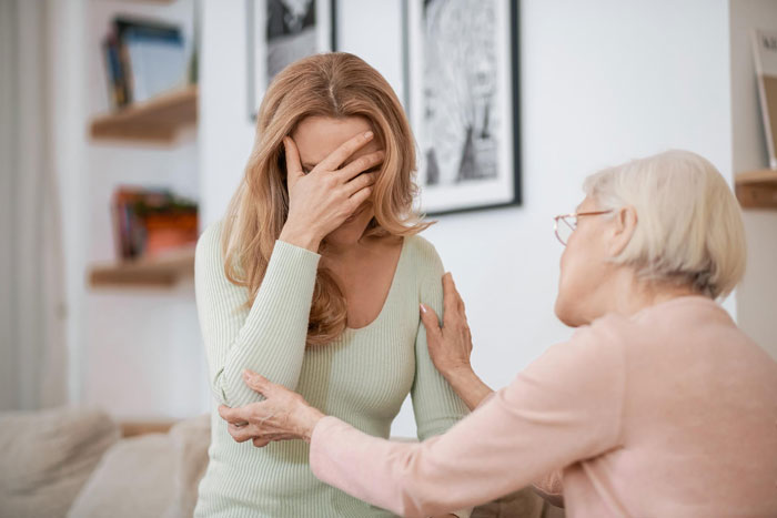 Young daughter-in-law upset and covering her face while overbearing mother-in-law tries to comfort her during a tense photoshoot discussion.