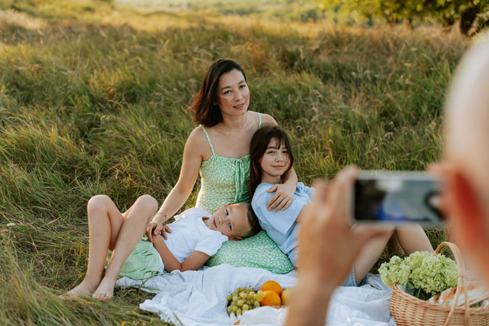 Mother and children having a photoshoot outdoors, capturing moments after a new birth while father takes a picture.